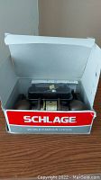 Open Schlage branded box showing door knob lock set including two round bronze knobs and lock mechanism.
