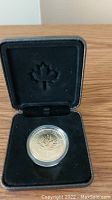 Open black display case with coin in clear capsule inside, visible maple leaf embossing on the lid interior.