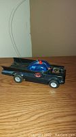 Side view of vintage black Batmobile toy with blue canopy and antenna wires, showing Batman logo on side.