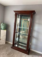 Front view of vintage solid wood curio cabinet showing glass shelves and carved wood frame.