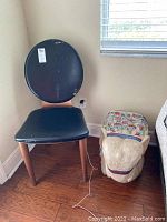 Photo showing vintage chair with black seat and backrest, wooden legs, next to carved wooden elephant statue.