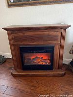 Front view of wooden freestanding electric fireplace with glowing flame effect in insert.
