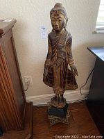 Full view of tall carved wooden statue on brass stand