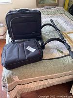 Two black laptop cases lying on bed: a Samsonite rolling case with wheels and a Swiss Gear laptop bag with visible handle.