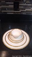 Stack of matched Lenox Tuxedo pattern dinnerware pieces (cup, saucer, salad plate, and dinner plate) showing gold band design.