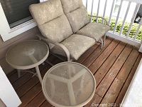 Photo showing the two-seater love seat glider with floral-patterned cushions and two round glass-top side tables on a wooden deck porch.