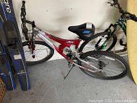 Full side view of the Mongoose mountain bike leaning against a wall showing red and silver frame with front suspension fork and knobby tires.