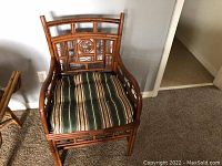 Front view of the bamboo and cane arm chair with striped cushion, showing carved geometric patterns on the backrest and sides.