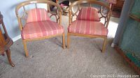 Pair of vintage wooden armchairs with rounded backrests and striped silk shantung seat cushions and pillows, placed on carpet.