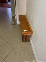 Long narrow wooden bench positioned against a wall showing weathered wood condition and simple rustic design.