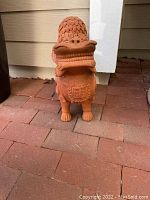 Front view of terracotta Foo dog statue on brick surface showing face, mane, and legs.