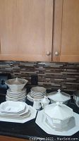 Wide view of stacked plates, covered casserole dishes, large platter and cups on counter showing entire set.