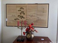 Full view of the silk oriental screen above a table with brass candelabra and brass vase with faux flowers.