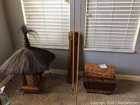 Full view of Polynesian thatched decor, African drum, bamboo storage chest, and two tall decorative arrows placed against a wall under windows.