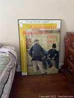 Framed Van Gogh Museum Amsterdam poster with visible text and artwork showing two gentlemen, view of entire poster leaning against wall next to furniture.