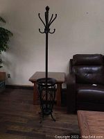 Full view of the black metal coat and umbrella holder standing in a room near furniture