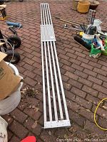 Full view of aluminum plank laid out on brick surface showing slatted design and end brackets