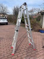 Full view of Featherlite multi-position ladder standing open on brick ground outdoors.
