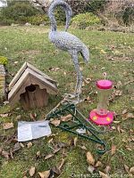 Full view of garden lot items on grass including metal bird sculpture, wooden birdhouse, hummingbird feeder, and metal plant hangers