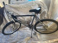 Full side view of the Kuwahara mountain bike showing the entire frame, tires, and seat. The bike has a kickstand and one visible pedal, with the other pedal missing.