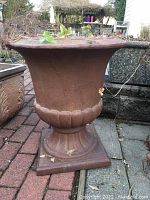 Side view of reddish-brown clay urn-shaped planter with scalloped base, sitting on brick patio.