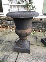 Side front view of black metal planter showing overall design and patina on patio surface.