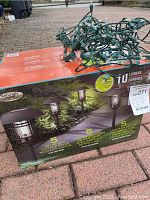 Box of Naturally Solar LED vintage style pathway lights with green string light on top.