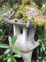 Close-up side angle view of the concrete Asian pagoda with moss on the roof and surrounded by garden plants.