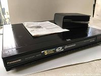 Panasonic DVD/CD player with 5-disc changer and labels on top surface, along with operating instructions and a black zippered CD case on top.