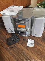 Panasonic stereo system with two speakers, remote control, and manual shown on wooden floor.