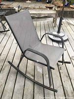Side view of the grey metal frame rocking chair on a wooden deck, showing the mesh seating and rocking base.