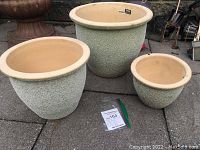 Set of three ceramic garden planters of varying sizes placed outdoors on pavement.