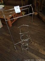 Full view of metal towel rack and toilet paper holder on floor showing structure and design.