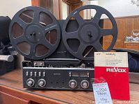 Front view showing two tape reels mounted on recorder, manual leaning against unit