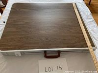 Folded table top closed with handle visible and measuring ruler beside it showing approximate 60 inch length.