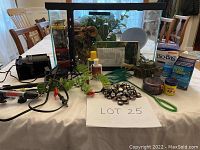 Full view of glass aquarium with mesh lid and assorted aquatic and reptile supplies arrayed on table including water treatments, nets, gravel, and heat lamp bulb.