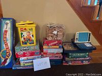 Shows the complete lot of 20 toys including LEGO Duplo bucket, Take Off board game, Yahtzee, wooden blocks, and stacked board games.