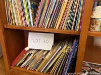 Shelf with multiple stacks of children's books arranged upright and lying down showing a variety of colorful covers and worn condition.