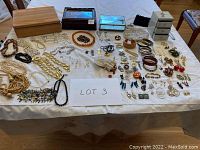 Full overview of assorted costume jewelry and jewelry boxes laid out on white sheet.