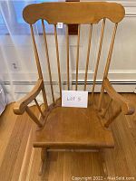 Front view of solid wood rocking chair showing high spindle back and armrests on hardwood floor.