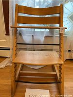 Front view of Tripp Trapp chair showing scratches, water damage on wooden seat and legs, black rods across front with one bent.