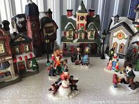 Whole porcelain lighted Christmas village set with various buildings and figurines placed on a white surface.
