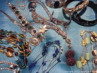 Various costume jewelry pieces laid on blue fabric. Includes necklaces, earrings, bracelets and bangles in assorted styles and colors.