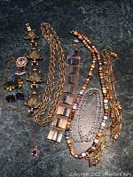 Top-down view of assorted costume jewelry laid out on a dark green marbled surface including various necklaces, bracelets, and earrings.