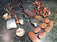 Photo of assorted necklaces showing 7 unique pieces made of wood, stone, shell and cord/strings, details of pendants and beadwork visible.