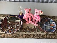 Lot contents including two decorative plates and two pink TY Beanie Babies placed on a patterned surface