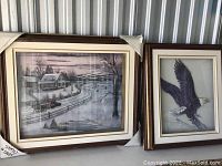 Two framed 3D art pieces shown side by side. Left piece depicts winter farmhouse scene; right piece shows eagle in flight.
