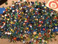 Pile of assorted glass marbles on beige carpet with cloth storage bag