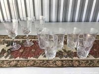Set of eight crystal glasses, four stemmed and four stemless, arranged on a fabric runner showing front and side views with etched patterns visible.