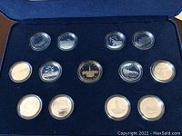 Open blue velvet presentation case interior showing 12 silver commemorative quarters in clear capsules arranged in an outer ring around central commemorative dollar coin.